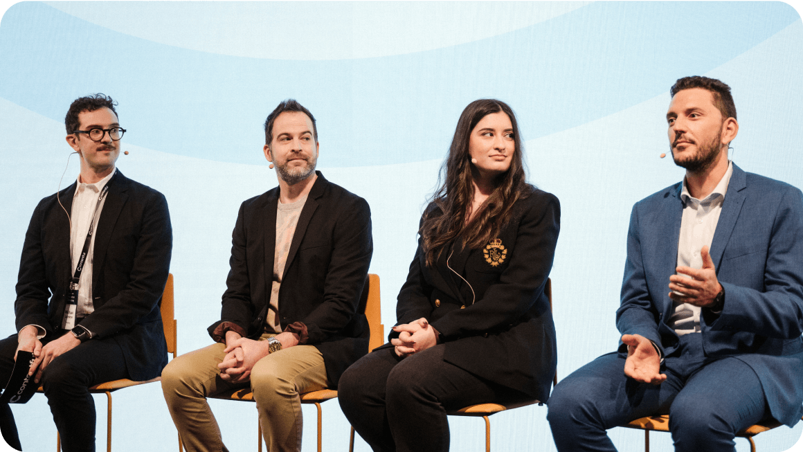 Four business professionals seated on orange chairs during a panel discussion against a light blue background