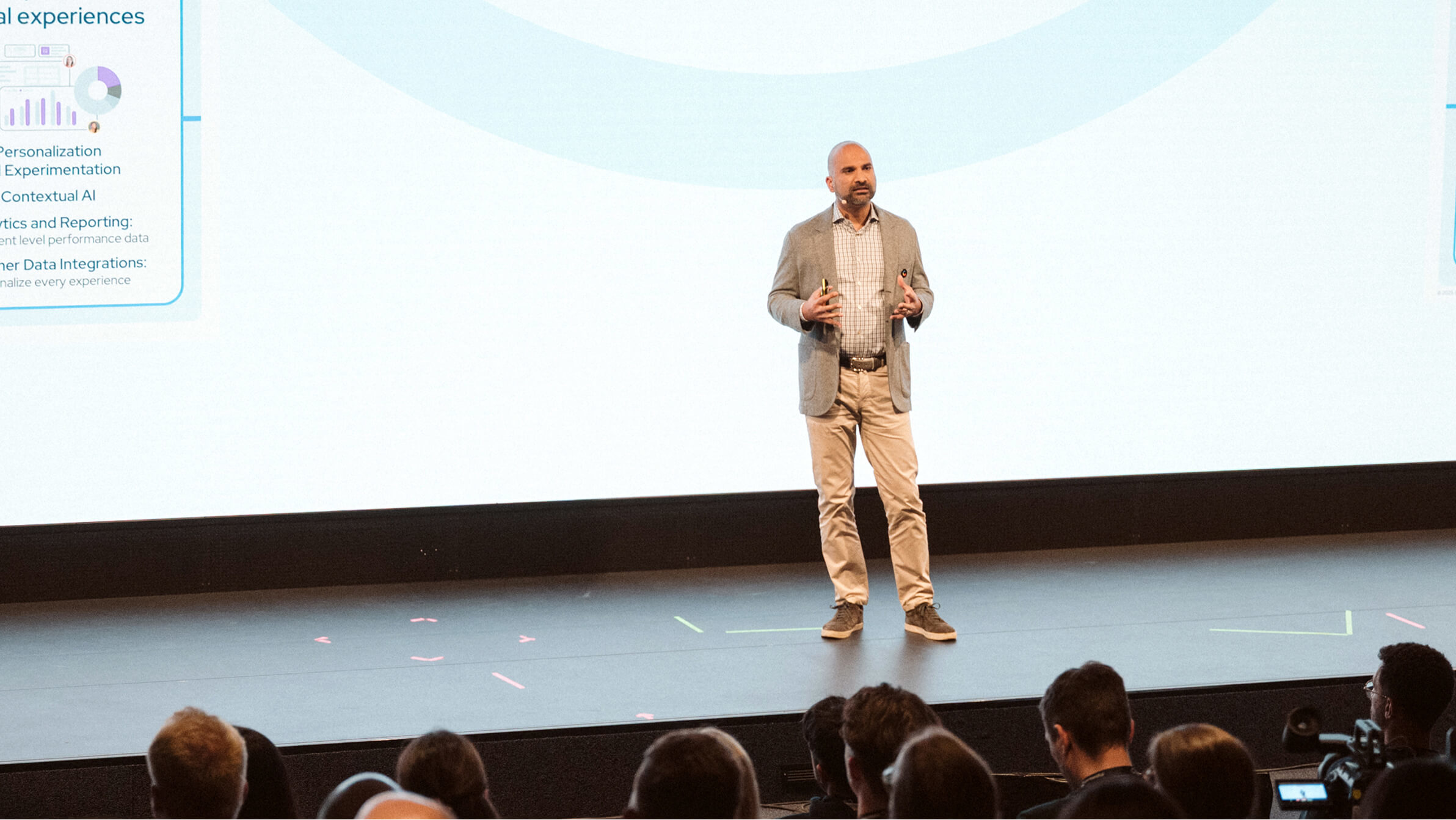 Contentful CEO Karthik Rau in business casual attire presenting on stage to an audience, with cameras recording the presentation
